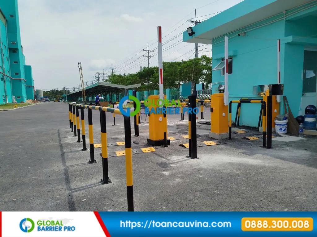 Hệ thống kiểm soát xe ra vào cho doanh nghiệp: triển khai thế nào? 6 Lối vào nhiều làn với hai hộp barie vàng và cột phân làn trước tòa nhà màu xanh