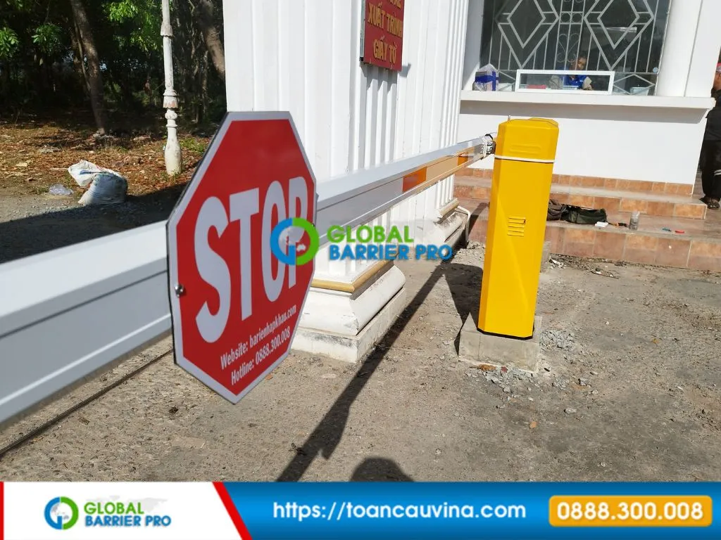 Cận cảnh cần barie trắng với biển STOP và thùng barie vàng